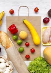 Variety of healthy food with paper bag on white wooden table, overhead. Cooking food background. Fresh fruits, vegetables, greens, meat. Top view, flat lay, from above. Shopping concept.