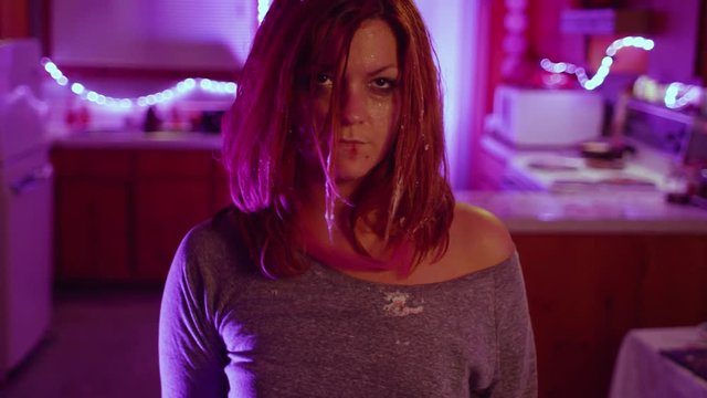 Point of view of the victim as a disheveled woman stabs with a knife them while standing in the kitchen