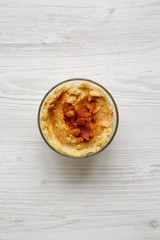 Bowl of Hummus with chickpeas, paprika and olive oil on a white wooden surface, top view. From above, overhead, flat lay.