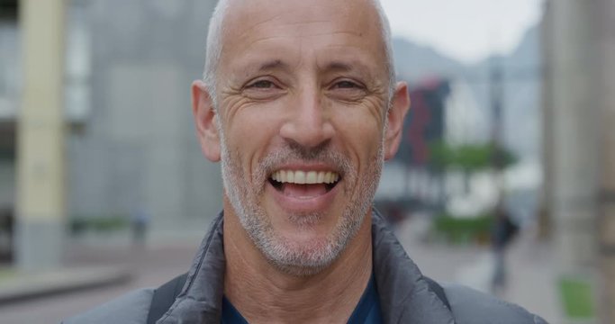 close up portrait attractive mature caucasian man laughing happy in city enjoying successful travel lifestyle middle aged commuter in urban background slow motion