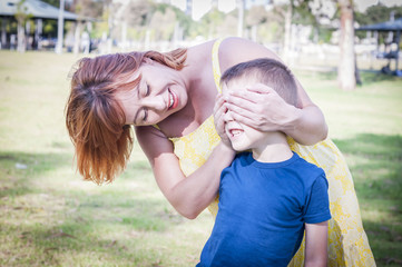 Young Caucasian woman closing her son's eyes standing behind him and he is trying to guess who is it.