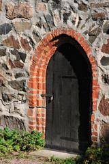 Fototapeta na wymiar Old dark wooden door in medieval castle stone wall.