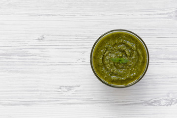 Bowl of freshly made basil pesto on white wooden table, view from above. Copy space.