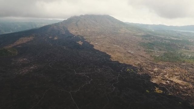 Mountain landscape with volcano, traces of lava on the ground, sky with clouds. Aerial view of Mount Batur Volcano in Kintamani. Bali volcano, also referred to as Kintamani is popular sightseeing