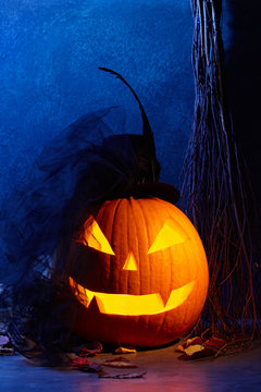 Halloween pumpkin head jack lantern with black bride hat in dark barn, holiday concept