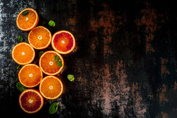 Fresh raw blood oranges, halves, with mint, on dark rusty background copy space top view