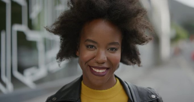 portrait of confident african american woman smiling cheerful looking at camera in vibrant urban city background young female student with funky afro slow motion
