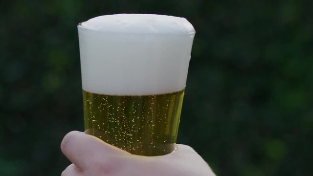 SLOW MOTION video raising a filled glass of beer with blurred background