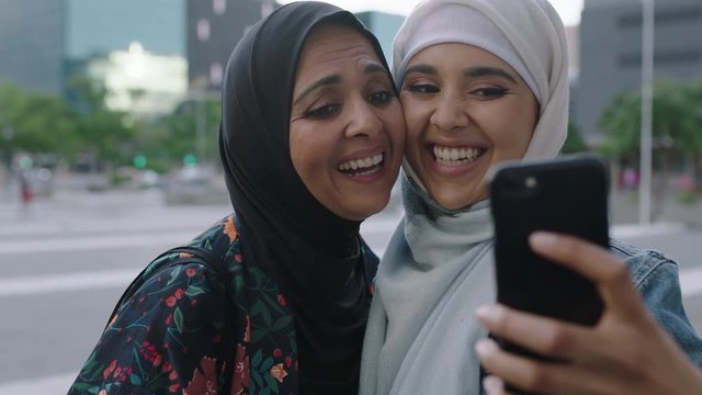 close up portrait of muslim mother and daughter smiling cheerful making faces posing taking selfie photo using smartphone in urban city