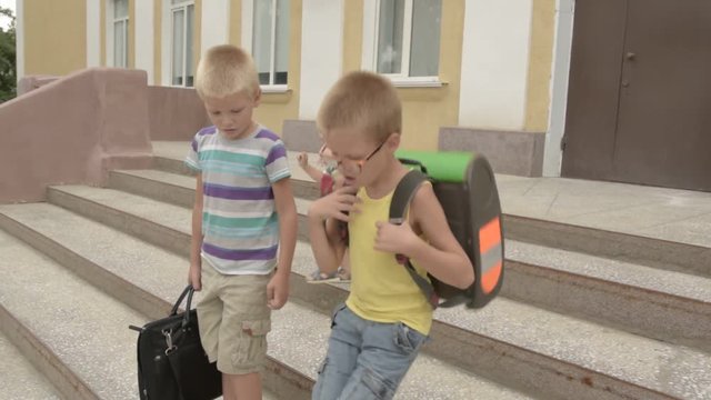 Happy pupil children go back to school. Start new education year after vacation. Boys and his little brother with bags are playing near school building. Education for kindergarten and preschool kids