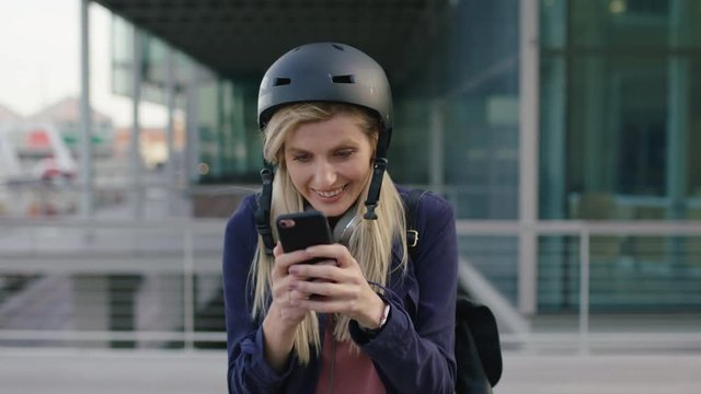 portrait of young cute blonde business woman intern wearing helmet texting browsing social media using smartphone in city