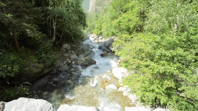 SLOW MOTION Watching a waterfall flow with blue skies and clouds in the mountains near Auron, France.