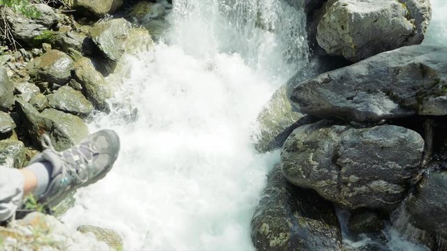 SLOW MOTION Watching a waterfall with the foot of a hiker in the foreground near Auron, France.