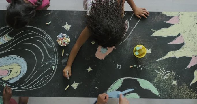 multi ethnic children drawing coloring space pictures together on blackboard using chalk happy kids enjoying fun creativity top view
