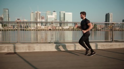 Man jogging in slow motion with Canary Wharf in the background.