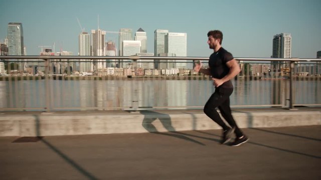 Man jogging in slow motion with Canary Wharf in the background.
