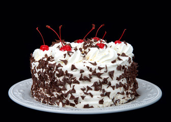 black forest cake on an off white plate isolated on a dark background. Whipped cream, shaved...
