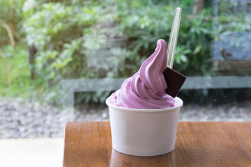 A cup of Purple Sweet potato soft serve or ice cream on wood table with blur green tree background.