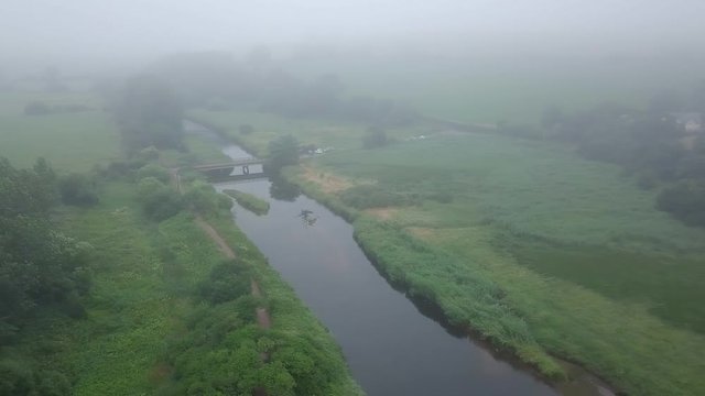LEFT TO RIGHT PANNING VIDEO of bridge crossing small river during foggy conditions.