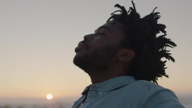 portrait of young african american man enjoying successful lifestyle achievement arms raised calm peaceful freedom concept ocean seaside background