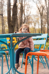 A child girl is sitting at a table outdoors against a background of a spring park