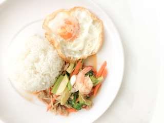 Fried Savory sauteed mixed vegetables with shimp and fried egg served with rice in white dish on white background as Thai homemade meal or recipe in the restaurant. Thai style food.