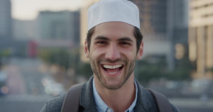 portrait happy young arab businessman laughing enjoying successful urban lifestyle in city at sunset wearing muslim kufi hat slow motion