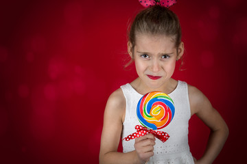 Girl shows mixed emotions on eating prohibited sweets: large multicolor lollipop