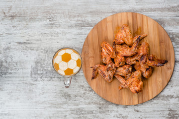 beer mug with a football on a beer foam near fried chicken wings. Top view