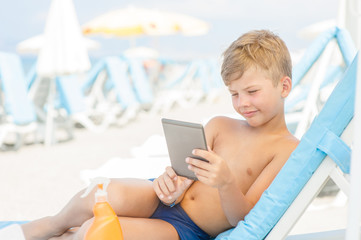 Little boy reading on electronic book on summer beach.  Relaxation resting vacations concept