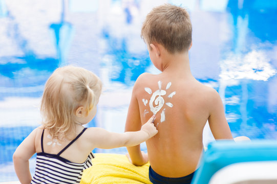 little girl draws the sun on her brother's back with sunscreen. Summer vacation concept