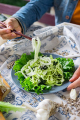 Woman hands holds and twirls zucchini spaghetti with chopsticks, raw vegan pasta with avocado sauce and salad leaves on plate. Vegan dinner, vegetarian lunch, healthy food