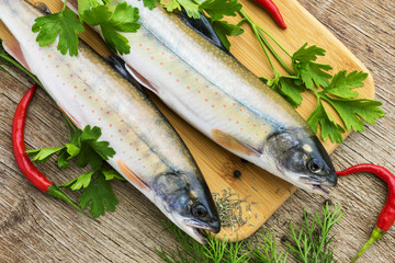 two fresh uncooked fish one kind of salmon with aromatic herbs on wooden cutting board