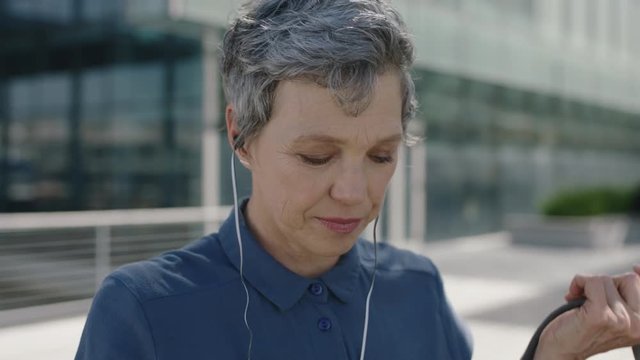 portrait of mature independent business woman listening to music using earphones wearing backpack in city