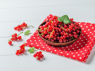 Fresh red currant with leaves on a bright fabric on a white wooden table.