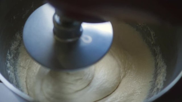 Inside a large mixer beating folding whisking dough in slow motiion