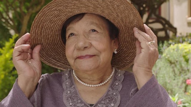 portrait of beautiful elderly woman in garden smiling looking up wearing hat pearl necklace
