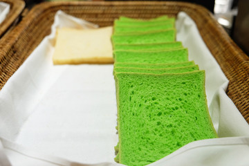 Rows of fresh white and green pandan sliced square bread on rattan rectangular basket