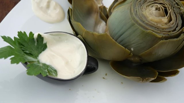 Eating cooked artichoke leaves with sauce