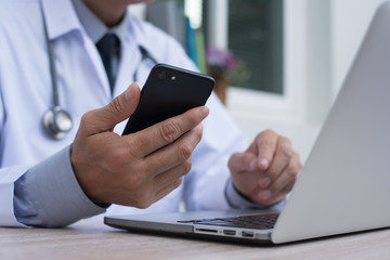 Doctor using smartphone and working on laptop computer