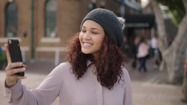 portrait of pretty mixed race girl wearing beanie hat posing taking selfie photo using smartphone