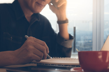 Businessman writing on notepad using smartphone
