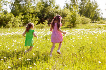 two little girls run across the field on a summer evening