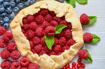 Homemade raspberry tart with mint leaves close up on the gray concrete background. Vegetarian healthy galette decorated with fresh blueberries and raspberries. Delicious dessert. Top view