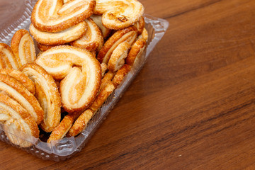 Palmier biscuits - french cookies made of puff pastry (also called palm leaves, elephant ears or french hearts) packed in plastic box on wooden table
