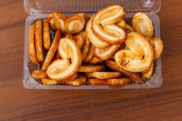 Palmier biscuits - french cookies made of puff pastry (also called palm leaves, elephant ears or french hearts) packed in plastic box on wooden table