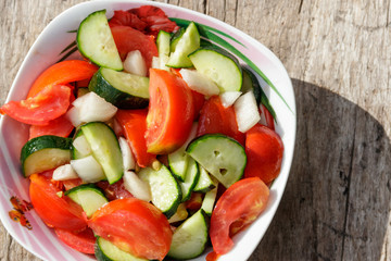 Fresh vegetable salad  with tomatoes, cucumbers, onion and olive oil on wooden table. Top view