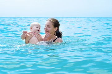Happy mother  bathing her baby in azure sea water