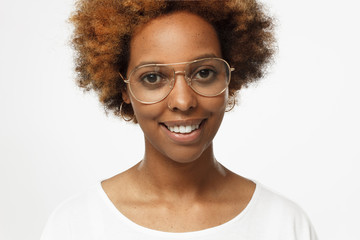 Studio close up portrait of young smiling cheerful dark skin african american woman wearing white t shirt and golden glasses, isolated on gray background