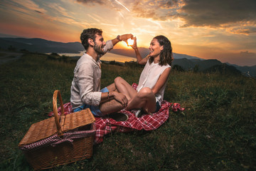 Portrait of young couple having good times on a picnic date, behind them is a beautiful sunset over Boka Bay - obrazy, fototapety, plakaty